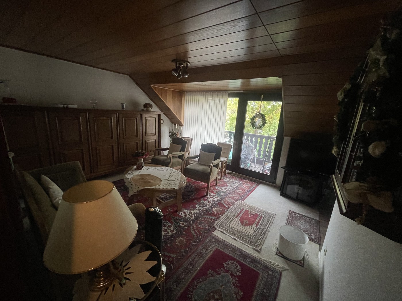 Dachgeschosswohnung Bad Rothenfelde vor der Entrümpelung – vollständig eingerichtetes Wohnzimmer mit Holzschrank, Sesseln, Teppichen, Lampe und Deko