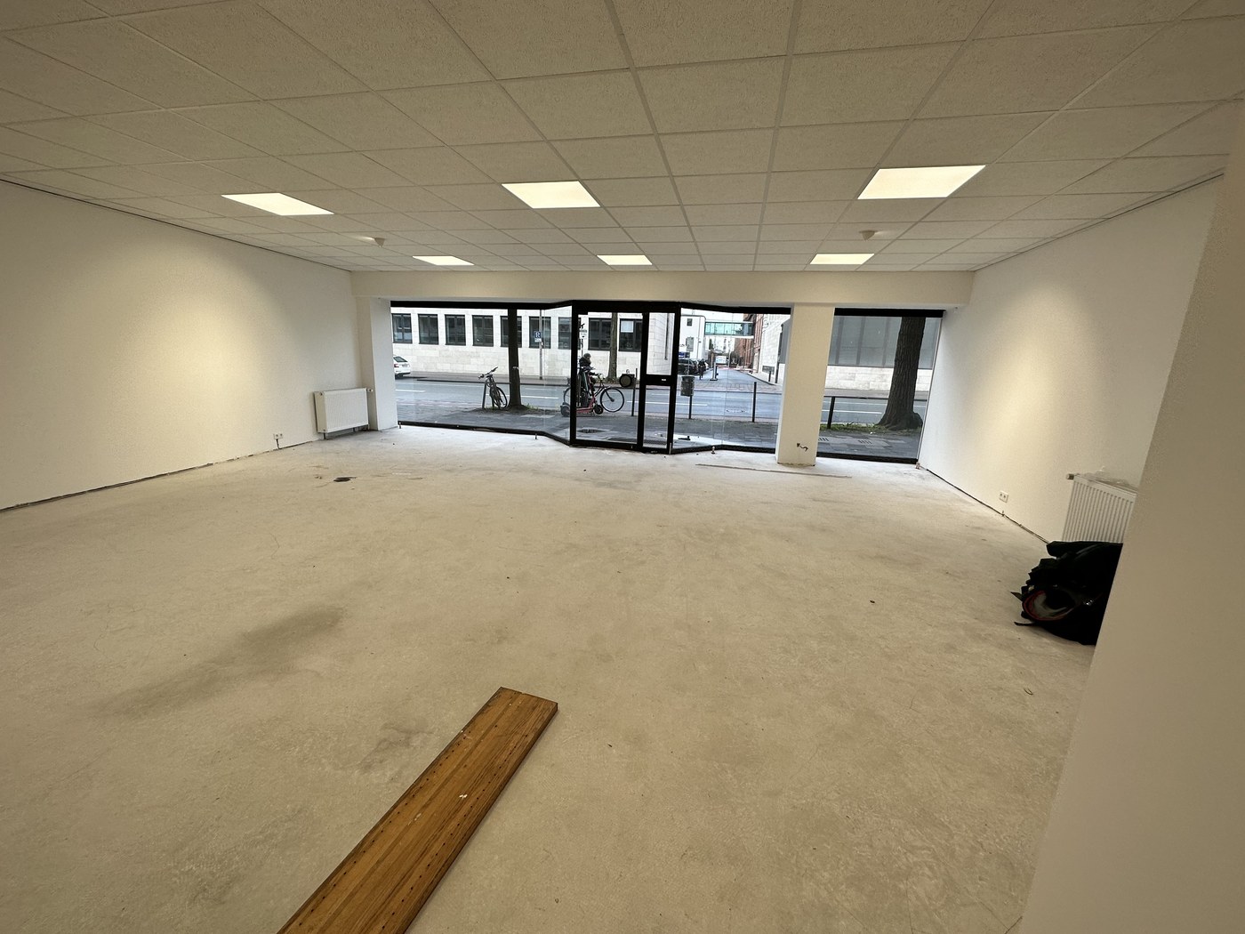 Maklerbüro Münster vor der Renovierung – leerer Raum mit altem Rohboden, Panoramafenster zur Straße, Wände bereits frisch gestrichen